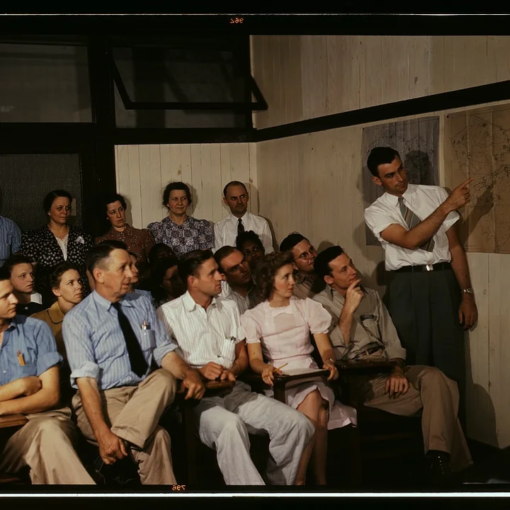 A presenter points to a wall map while a group studies the larger situation.