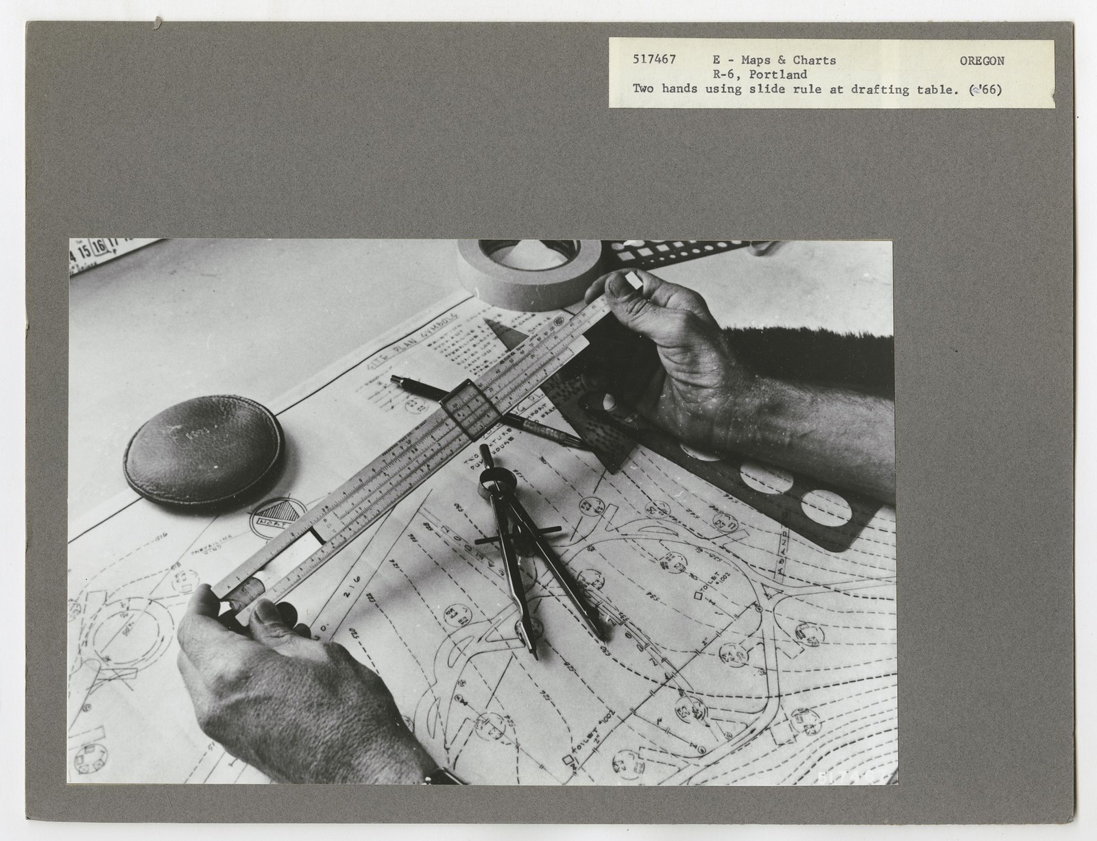 Hands using a slide rule over a map, with a compass and drafting tools on the table, circa 1966.