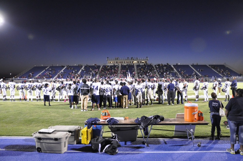 Players gathered along the sideline facing the field and stadium stands before a Texas high school football game.